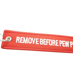 May include: Red fabric keychain with a silver ring and the text "REMOVE BEFORE PEW PEW" in white.