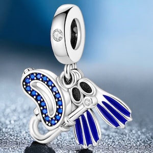 Könnte beinhalten: Silberner Charm mit einem Thema zum Tauchen. Der Charm zeigt ein Paar blaue und silberne Flossen, eine Tauchmaske und eine blaue und silberne Luftflasche. Der Charm hat einen kleinen, klaren Edelstein oben und auf den Flossen.