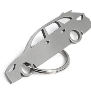 Peut inclure: Un porte-clés argenté en forme de voiture. Le porte-clés est découpé pour montrer les fenêtres et les roues de la voiture. Un porte-clés argenté est attaché à la carrosserie de la voiture. Le porte-clés est en métal et sur fond blanc.