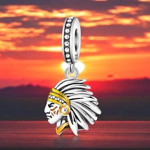 May include: Silver charm featuring a Native American chief wearing a headdress with gold accents. The charm is designed to be used on a bracelet or necklace.