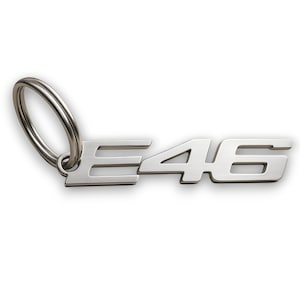 May include: A silver metal keyring featuring the letters and numbers "E46". The keyring has a split ring for attaching keys. The font used for the letters and numbers is sans-serif.