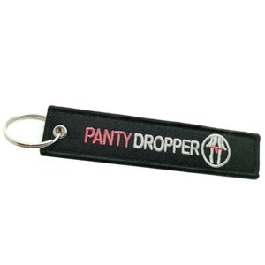 Peut inclure: Porte-clés noir avec un motif brodé blanc et rose qui dit "Panty Dropper" avec un cercle autour d'une image stylisée de jambes de femme.