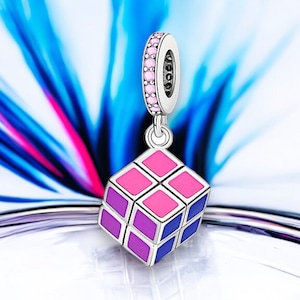 May include: A silver charm in the shape of a Rubik's Cube with pink, purple, and blue squares. The charm has a silver ring with pink stones around it.