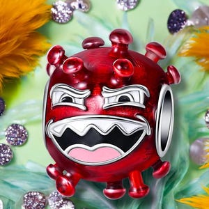 Puede incluir: Un charm rojo con una cara de dibujos animados, con una amplia sonrisa y ojos enojados. El charm tiene forma redonda con púas que sobresalen y un anillo plateado. El fondo incluye plumas amarillas y adornos brillantes.