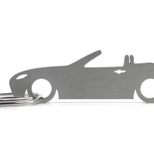 Puede incluir: Un llavero de metal plateado con forma de coche descapotable. El llavero tiene un anillo.