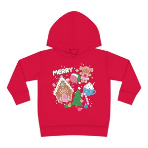 Może przedstawiać: Czerwona bluza z kapturem dla małych dzieci z motywem świątecznym przedstawiającym domek z piernika, piernikowego ludzika, laskę cukrową, kubek gorącej czekolady, choinkę i napis "Merry".