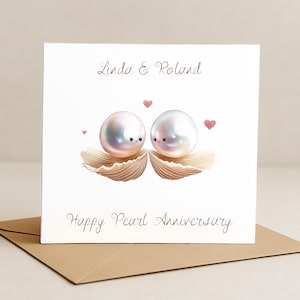 Op de afbeelding: Een witte wenskaart met de tekst "Linda & Roland" en "Happy Pearl Anniversary". De kaart toont twee cartoonparels met gezichten, rustend in zeeschelpen, met roze hartjes. De kaart ligt op een bruine envelop.