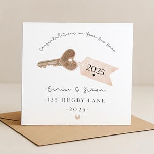 Puede incluir: Tarjeta cuadrada con una ilustraci&oacute;n de una llave con cabeza en forma de coraz&oacute;n y una etiqueta que dice "2025". La tarjeta dice "Felicitaciones por tu nuevo hogar" e incluye los nombres "Eunice & Simon" y la direcci&oacute;n "125 Rugby Lane."