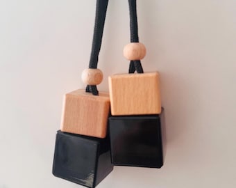 May include: Two hanging car air fresheners. Each freshener has a black square base topped with a natural wood square and a wooden bead. The fresheners hang from a black cord.