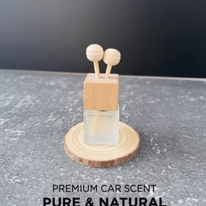 May include: A car air freshener with a wooden top and two round wooden diffusers. The freshener sits on a small wooden slice and has the words "PREMIUM CAR SCENT PURE & NATURAL" printed on the bottom.