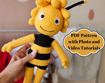 May include: Crocheted bee plush toy with black and yellow stripes, a smiling face, and antennas. The toy is being held by a hand. The text "PDF Pattern with Photo and Video Tutorials" is in a speech bubble.
