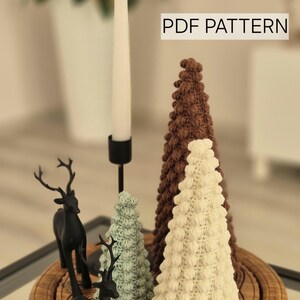 May include: A set of three crocheted Christmas trees in brown, white, and green, with two black deer figurines on a wooden base. The text "PDF PATTERN" is visible in the top right corner of the image.