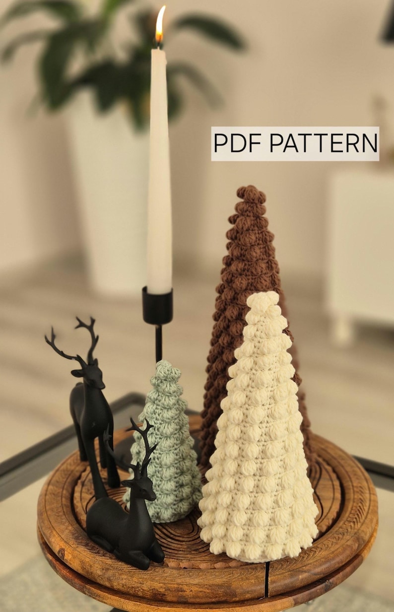 May include: A set of three crocheted Christmas trees in brown, white, and green, with two black deer figurines on a wooden base. The text "PDF PATTERN" is visible in the top right corner of the image.
