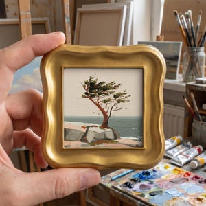 May include: A small square painting in a thick, ornate gold frame depicting a windswept tree on a rocky coastal cliff overlooking a calm sea. The artwork features a muted colour palette of greens, browns, and greys, capturing a landscape scene.
