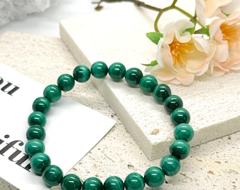 May include: A circular bracelet composed of polished, spherical malachite beads featuring distinct dark and light green banded patterns. The beads are strung together in a continuous loop, showcasing the natural, deep green mineral variations.