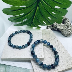 Könnte beinhalten: Zwei blaue Edelstein-Armbänder mit runden Perlen. Die Armbänder liegen auf einer weißen, strukturierten Oberfläche.