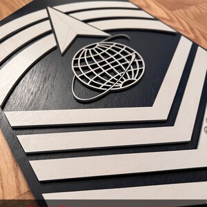 May include: A wooden plaque featuring a layered design with a dark blue base and white accents. The design includes chevrons, an arrow, and a globe with lines. The text "SVG PDF DXF" is at the bottom.