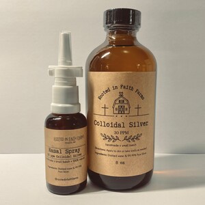 Op de afbeelding: Twee bruine glazen flessen met etiketten. De grotere fles is gelabeld "Rooted in Faith Farms Colloïdaal Zilver 30 PPM handgemaakt kleine batch Gebruiksaanwijzing: Aanbrengen op de huid of oraal innemen indien nodig Ingrediënten: Gedistilleerd water & 99,99% puur zilver 8 oz". De kleinere fles is gelabeld "Rooted in Faith Farms Neusspray 30 ppm Colloïdaal Zilver handgemaakt kleine batch 100% natuurlijk Ingrediënten: Gedistilleerd water & 99,99% puur zilver @rootedinfaithfarms".