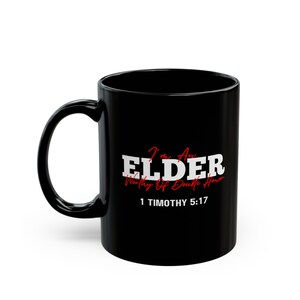 Może przedstawiać: Czarny ceramiczny kubek do kawy z białym tekstem, który brzmi "I'm An ELDER Worthy Of Double Honor 1 TIMOTHY 5:17". Tekst "ELDER" jest czerwony.