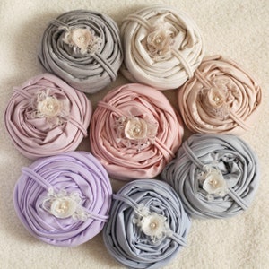 May include: Set of 8 fabric wraps in various colors, including light pink, lavender, gray, and beige. Each wrap is made of a soft, stretchy fabric and features a delicate lace flower embellishment.