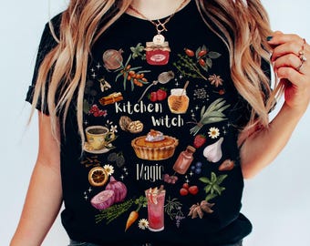 Könnte beinhalten: Ein schwarzes Kurzarm-T-Shirt mit einem farbenfrohen Grafikdruck verschiedener Lebensmittel, Kräuter und Gewürze, die um den Text Kitchen Witch Magic angeordnet sind. Das Design enthält Illustrationen von einem Kuchen, Honig, Beeren und Zwiebeln.
