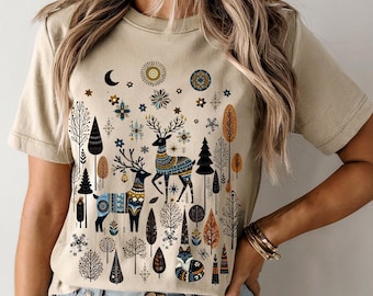 Puede incluir: Camiseta de color crema suave con una escena forestal caprichosa que presenta ciervos, árboles y elementos celestiales. El diseño incorpora detalles en azul, naranja y negro. El texto "SOFT CREAM" está en la parte inferior derecha.