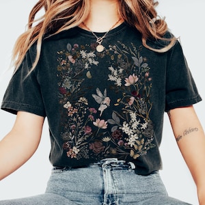 May include: Black t-shirt with a floral design featuring butterflies and flowers in pink, white, and purple. The shirt is worn with light blue jeans and white trainers. The word "Black" is printed at the bottom of the image.