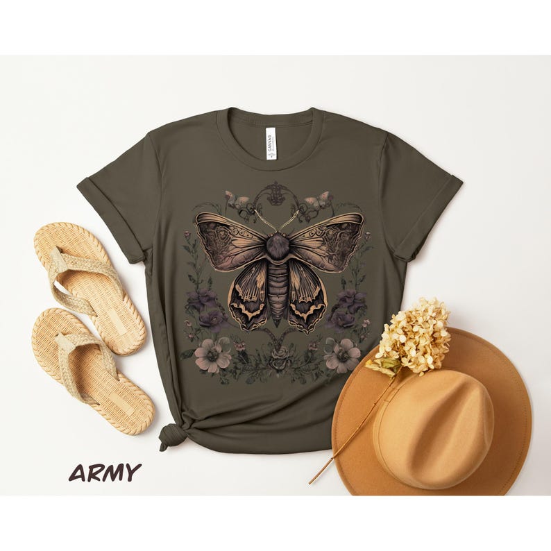May include: Army green t-shirt featuring a detailed moth illustration with floral accents. The design is in shades of brown and tan. A straw hat and woven sandals are also visible.