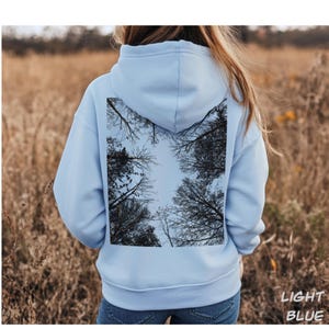 K&ouml;nnte beinhalten: Hellblauer Kapuzenpullover mit einem quadratischen Motiv eines Baumkronen-Himmels vor hellblauem Himmel. Der Text "LIGHT BLUE" ist unten rechts in Wei&szlig; gedruckt. Der Hoodie ist aus weichem Material.