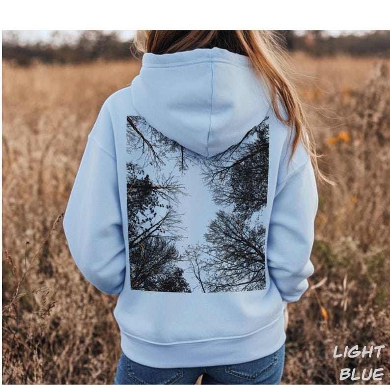 K&ouml;nnte beinhalten: Hellblauer Kapuzenpullover mit einem quadratischen Motiv eines Baumkronen-Himmels vor hellblauem Himmel. Der Text "LIGHT BLUE" ist unten rechts in Wei&szlig; gedruckt. Der Hoodie ist aus weichem Material.