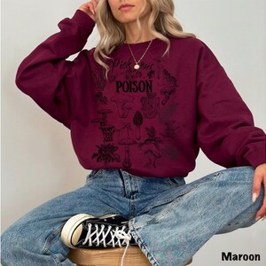 May include: Maroon sweatshirt with a black graphic design featuring mushrooms and the text "Pick Your Poison". The sweatshirt is a long-sleeved crew neck style.