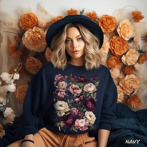Puede incluir: Sudadera azul marino con un diseño floral de peonías rosas, blancas y burdeos. La persona lleva un sombrero azul oscuro y pantalones cortos color beige. La palabra "NAVY" está impresa en blanco en la parte inferior derecha.