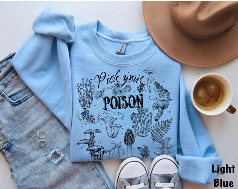 May include: Light blue sweatshirt with the text "Pick your POISON" and various mushroom illustrations in black. The sweatshirt is paired with light-wash denim jeans, a brown hat, and a cup of coffee.