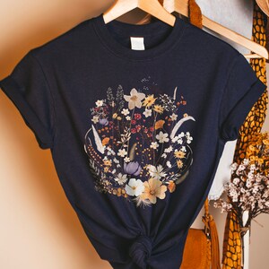 May include: A navy blue t-shirt with a floral print featuring dried flowers in shades of white, yellow, and purple.