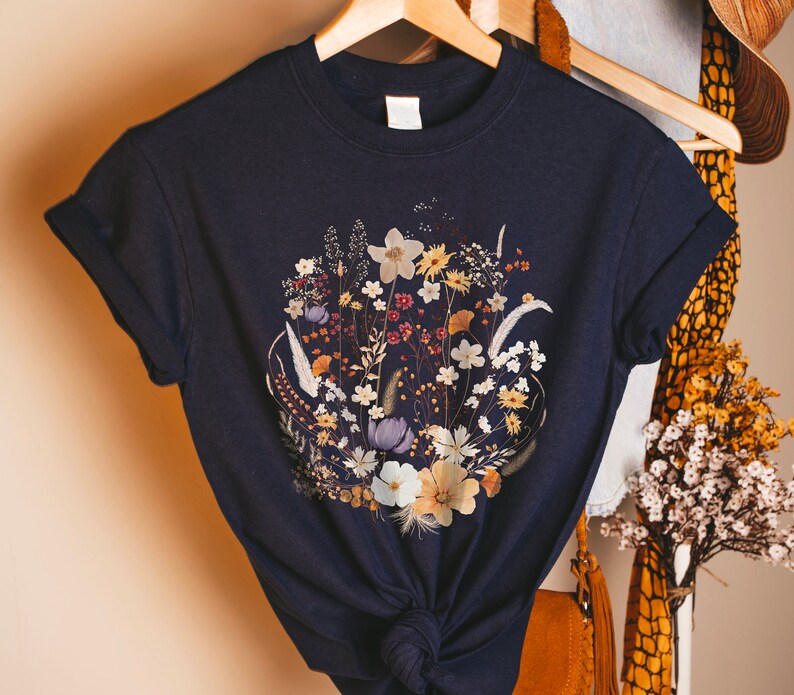 May include: A navy blue t-shirt with a floral print featuring dried flowers in shades of white, yellow, and purple.