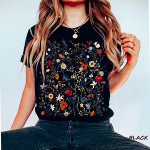 May include: Black t-shirt with a floral print featuring pressed flowers in various colors, including red, orange, yellow, blue, and white.