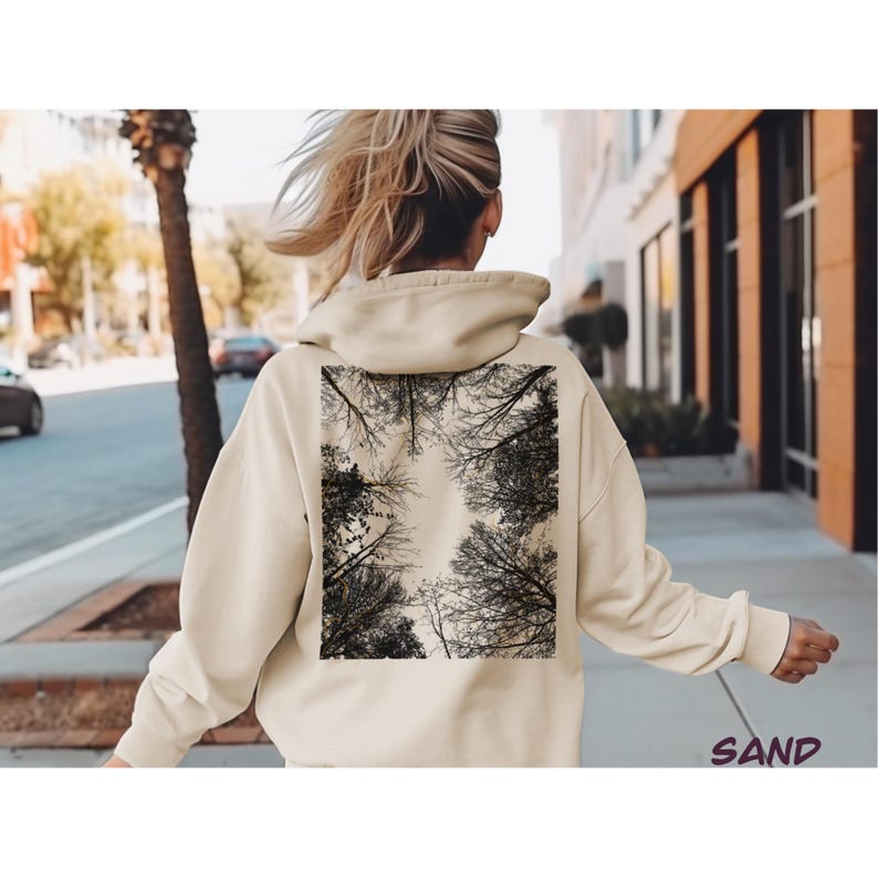 K&ouml;nnte beinhalten: Sandfarbener Kapuzenpullover mit einem schwarz-wei&szlig;en Astdesign auf dem R&uuml;cken. Der Hoodie hat eine Kapuze und lange &Auml;rmel. Das Wort "SAND" ist in kursiver Schrift in der unteren rechten Ecke des Bildes aufgedruckt.