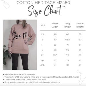 May include: A Cotton Heritage M2480 size chart featuring a dusty rose sweatshirt in size M. The chart lists chest width, body length, and sleeve length in centimeters for sizes XS through 3XL. Text includes model details and measurement instructions.