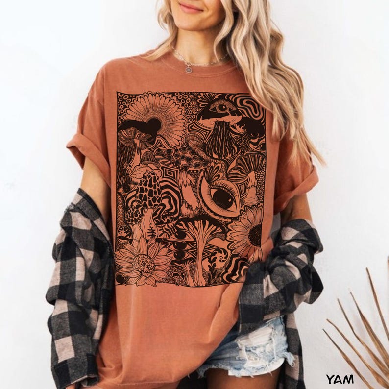 May include: A terracotta-colored short-sleeve t-shirt featuring a large, square black graphic print on the front. The design consists of detailed line art depicting various mushrooms, sunflowers, and stylized eyes arranged in a dense, intricate pattern.