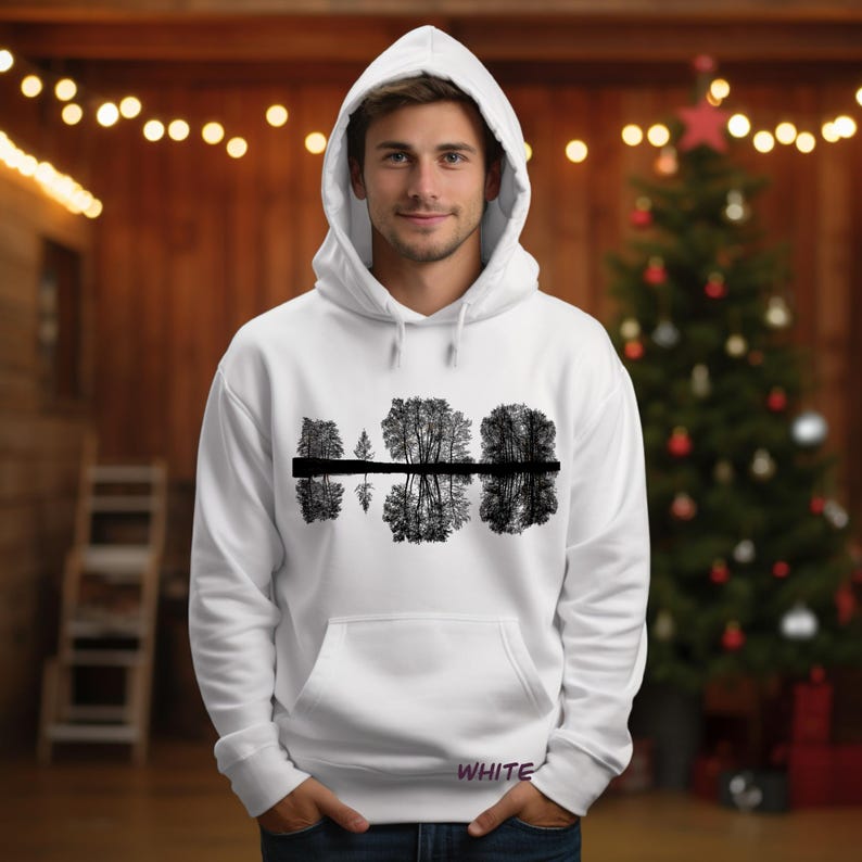 K&ouml;nnte beinhalten: Wei&szlig;er Kapuzenpullover mit einem schwarz-wei&szlig;en Baumreflexionsmuster. Das Wort "WHITE" ist unten in Lila aufgedruckt. Der Pullover hat eine Vordertasche und eine Kapuze mit Kordelzug.