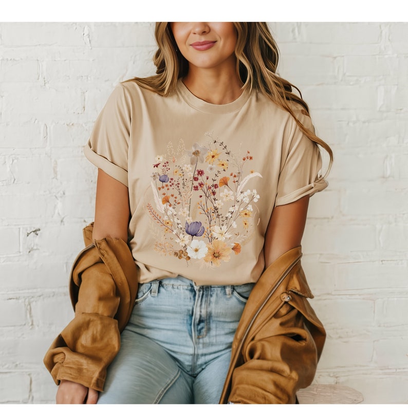 May include: A beige t-shirt with a floral print featuring a variety of flowers in shades of yellow, orange, red, purple, and white.
