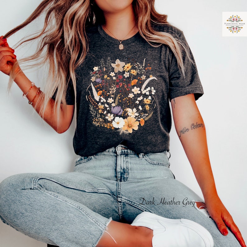 May include: A dark heather grey t-shirt with a floral print featuring a variety of flowers in shades of yellow, orange, purple, and white. The shirt has a crew neck and short sleeves.