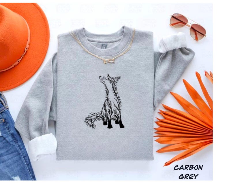 May include: A carbon grey crewneck sweatshirt featuring a black graphic of a fox composed of intricate tree branch silhouettes. The sweatshirt is displayed alongside an orange wide-brimmed hat, blue denim jeans, and brown-tinted sunglasses.