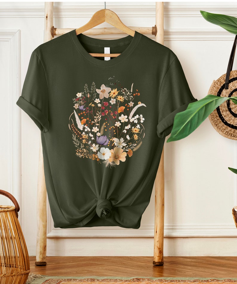 May include: A dark green t-shirt with a floral print featuring a variety of flowers in shades of white, yellow, orange, and purple.