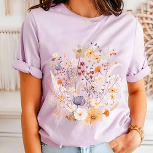 May include: A lavender t-shirt with a floral print featuring a variety of flowers in shades of yellow, orange, white, and purple.