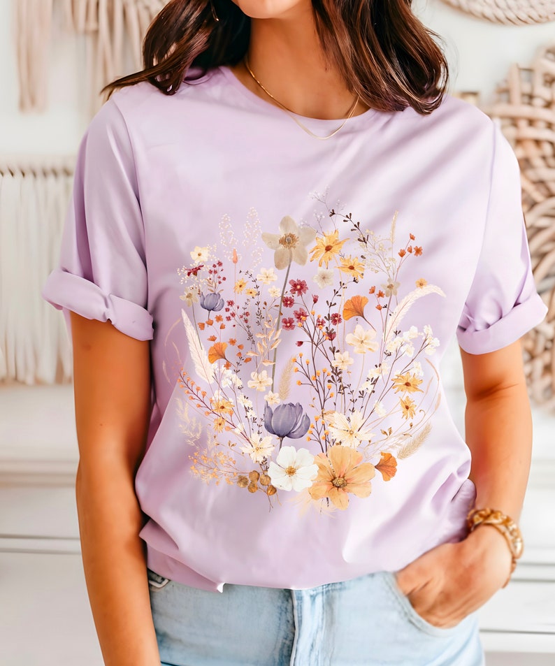 May include: A lavender t-shirt with a floral print featuring a variety of flowers in shades of yellow, orange, white, and purple.