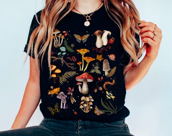 May include: Black t-shirt with a colorful mushroom and forest illustration. The illustration includes mushrooms, butterflies, leaves, acorns, and other forest elements.