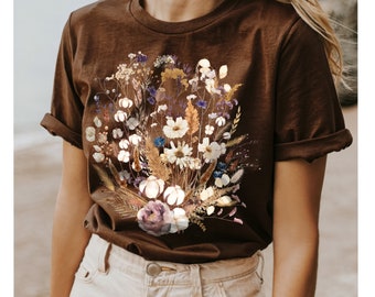 May include: A brown t-shirt with a floral print featuring a bouquet of dried flowers in shades of white, beige, purple, and blue.