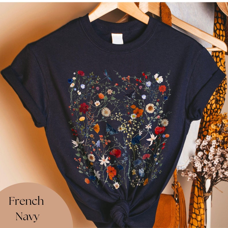 May include: A navy blue t-shirt with a floral print featuring a variety of flowers, leaves, and butterflies. The print is in shades of red, orange, yellow, white, and blue.