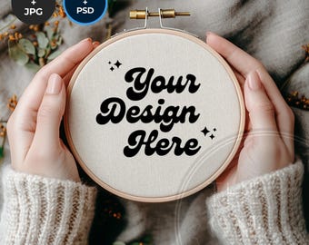 May include: A person is holding a white embroidery hoop with the text "Your Design Here" in black. The hoop is surrounded by a brown wooden frame.